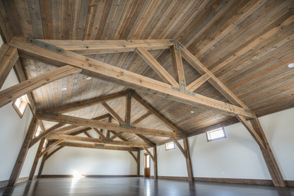 Weatherwood Beachwood Wooden trusses in a large open room with white walls and wooden flooring.
